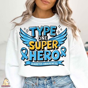 May include: White sweatshirt with blue and yellow text that reads "Type One Super Hero" with a blue ribbon and wings. The text "Diabetes Awareness" is below the main text.