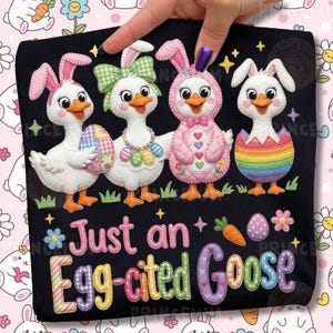 May include: Black t-shirt featuring four cartoon geese dressed as Easter bunnies. The geese are white with orange beaks and feet, wearing bunny ears and holding Easter eggs. Text reads "Just an Egg-cited Goose."