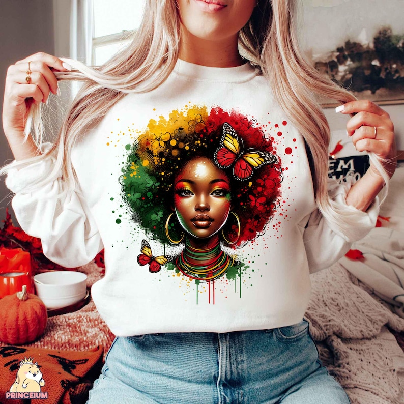 K&ouml;nnte beinhalten: Wei&szlig;es Sweatshirt mit einem bunten Grafikdruck einer Frau mit Afrofrisur, die eine Halskette und Ohrringe tr&auml;gt. Die Grafik ist von bunten Farbspritzern und Schmetterlingen umgeben.
