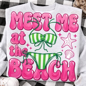 Puede incluir: Una sudadera gris claro con el texto "MEET ME at the BEACH" en letras rosas de burbujas. El diseño incluye un bikini a rayas verdes y blancas, una estrella de mar y una concha.