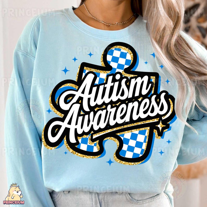 May include: Light blue sweatshirt featuring a gold glitter puzzle piece design. The puzzle piece has a blue and white checkered pattern and the text "Autism Awareness" in white.