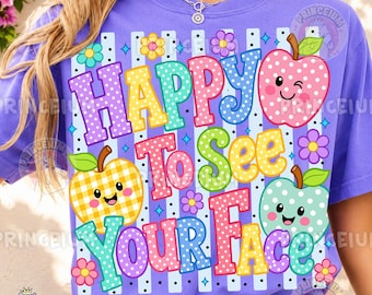 May include: A purple t-shirt featuring a graphic print with the text HAPPY TO SEE YOUR FACE. The design includes three smiling, patterned apples in pink, yellow, and light green, surrounded by colorful flowers and blue star accents.