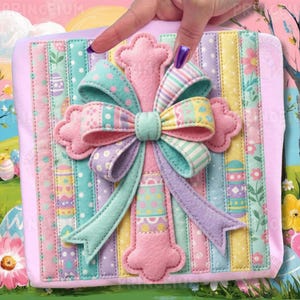 Könnte beinhalten: Ein pastellfarbenes, österliches Dekorationsstück. Es zeigt eine rosa Kreuzform mit einer großen Schleife in Türkis-, Rosa-, Lila- und Gelbtönen. Der Hintergrund ist ein Patchwork aus vertikalen Streifen in ähnlichen Pastellfarben, mit Punkten und Osterei-Designs.