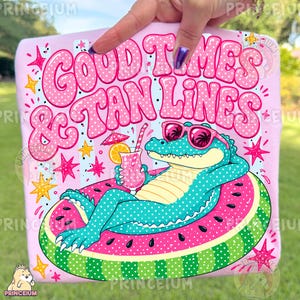 May include: A light pink t-shirt featuring a graphic of a teal alligator wearing pink sunglasses, lounging on a watermelon-patterned pool float while holding a tropical drink. The text reads GOOD TIMES & TAN LINES in large pink polka-dot letters.