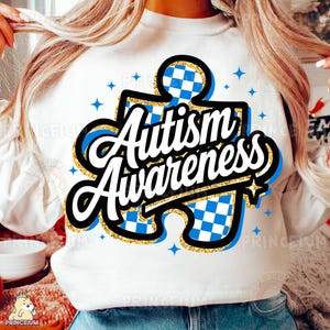May include: White sweatshirt featuring a blue and white checkered puzzle piece design. The puzzle piece has gold glitter and the words "Autism Awareness" in black and white.