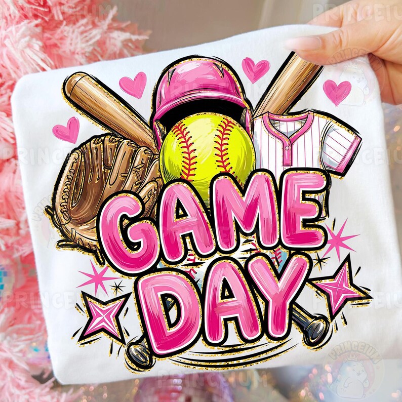 May include: White t-shirt with a softball design. It features a pink helmet, a yellow softball, a brown glove, and the words "GAME DAY" in pink bubble letters. Pink hearts and stars are also included in the design.