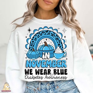 May include: White sweatshirt with a blue and black design featuring a rainbow, pumpkins, and a cup of coffee. The text reads "In November We Wear Blue for Diabetes Awareness."
