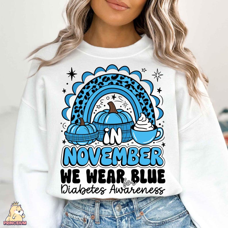 May include: White sweatshirt with a blue and black design featuring a rainbow, pumpkins, and a cup of coffee. The text reads "In November We Wear Blue for Diabetes Awareness."