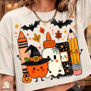 Può includere: Una t-shirt color crema con una stampa grafica raffigurante una zucca arancione sorridente con un cappello da strega, un fantasma bianco, una matita gialla, un pastello a cera arancione e una colla, circondati da pipistrelli neri e foglie.