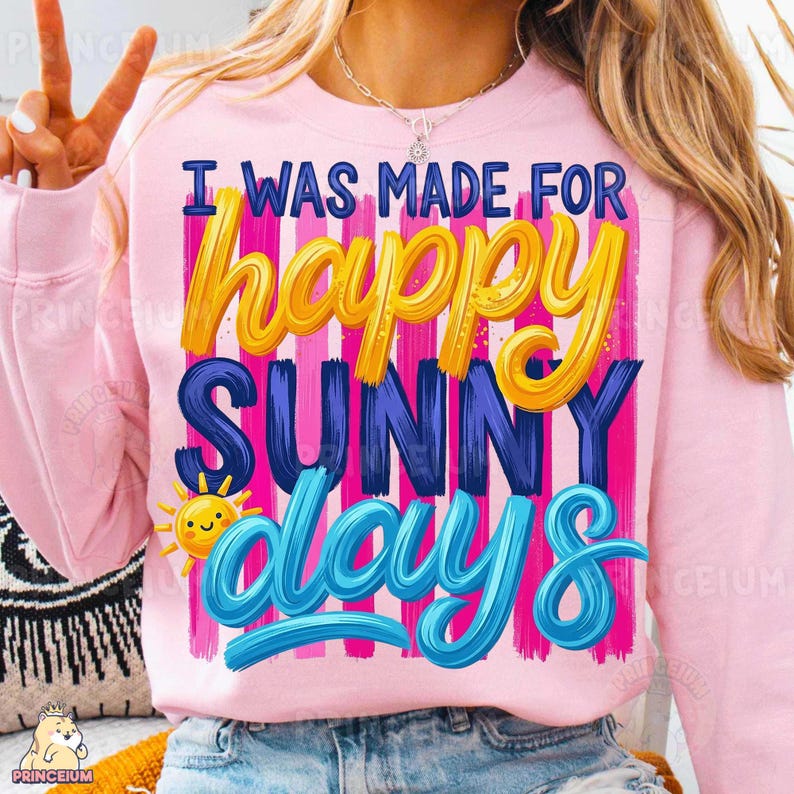 Może przedstawiać: Jasnor&oacute;żowa bluza z napisem "I WAS MADE FOR happy SUNNY days" w kolorze ż&oacute;łtym, niebieskim i białym. Projekt zawiera uśmiechnięte słońce i pionowe r&oacute;żowe i fioletowe paski.