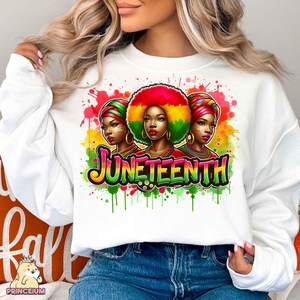 K&ouml;nnte beinhalten: Wei&szlig;er Pullover mit einem farbenfrohen Grafikdesign, das drei Frauen mit Afrofrisuren und das Wort "Juneteenth" in einer stilisierten Schrift zeigt. Das Design ist von bunten Farbspritzern umgeben.
