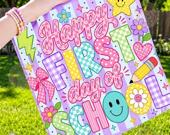 May include: A square sign with a light purple and white striped background featuring the text Happy First day of SCHOOL in colorful, patterned letters. The design includes a yellow star, a pink bow, a pencil, flowers, and a smiley face.