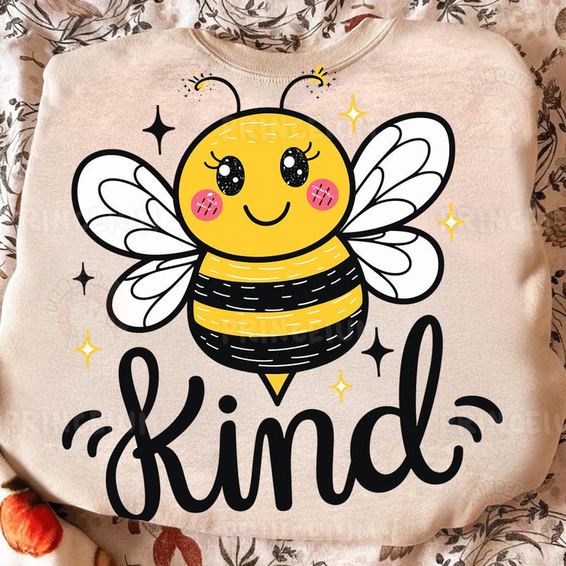 May include: A beige sweatshirt featuring a cartoon bee with a yellow body, black stripes, and white wings. The bee has a smiling face and the word "Kind" in black script below. The design includes stars and sparkles.
