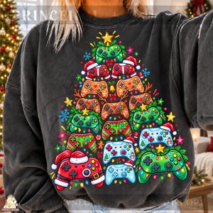 May include: A charcoal grey crewneck sweatshirt featuring a graphic print of a Christmas tree constructed from various colourful video game controllers, accented with Santa hats, stars, snowflakes, and string lights.