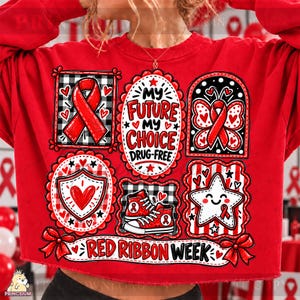Op de afbeelding: Een rood sweatshirt met lange mouwen en een grafische print met de tekst "MY FUTURE MY CHOICE DRUG-FREE" en "RED RIBBON WEEK". Het ontwerp bevat een rood bewustzijnslint, een vlinder, een hartschild, sneakers en een lachende ster.