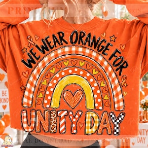 May include: An orange sweatshirt featuring a graphic of a rainbow with multiple patterns including plaid, polka dots, and glitter. The text "WE WEAR ORANGE FOR UNITY DAY" is printed in black. The design includes small heart and star icons throughout.