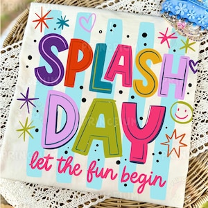 May include: A cream-colored t-shirt with the words "SPLASH DAY" in colorful, bold letters. The shirt features a light blue striped background and the phrase "let the fun begin" in pink script. Decorative stars, hearts, and a smiley face complete the design.