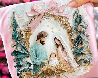 May include: Pink fabric with a textured painting of the Nativity scene. The artwork features Mary, Joseph, and baby Jesus, surrounded by a gold wreath, stars, and Christmas trees. A pink bow is at the top.