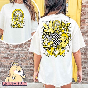 May include: White t-shirt with a yellow graphic on the back. The graphic includes a rainbow, hearts, butterflies, stars, and the text "Fight for a Cure".