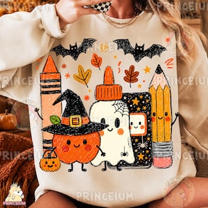Op de afbeelding: Een beige sweatshirt met een kleurrijke afbeelding van een krijtje, een lijmfles, een potlood, een pompoen met een heksenhoed en een spook. Het ontwerp bevat zwarte vleermuizen, oranje en bruine bladeren en kleine sterretjes op de stof.