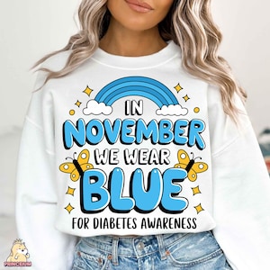 May include: White sweatshirt with a blue rainbow, clouds, and butterflies. The text reads "In November We Wear Blue For Diabetes Awareness."