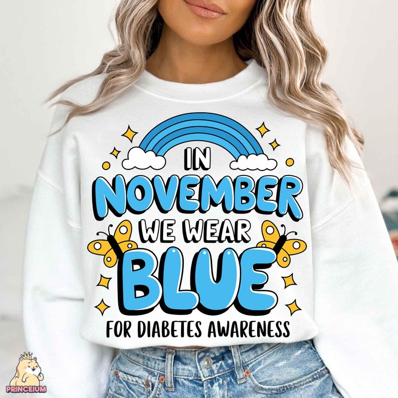 May include: White sweatshirt with a blue rainbow, clouds, and butterflies. The text reads "In November We Wear Blue For Diabetes Awareness."