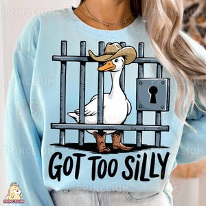 May include: A light blue sweatshirt with a cartoon image of a goose wearing a cowboy hat and boots. The goose is behind bars and the text "GOT TOO SILLY" is printed below the image.