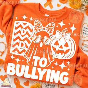 Puede incluir: Una sudadera naranja con un estampado gráfico blanco de un fantasma con lazo y gafas junto a una calabaza. El texto dice "BE KIND TO BULLYING" con un patrón de chevrón en la letra B. El diseño incluye detalles de estrellas.