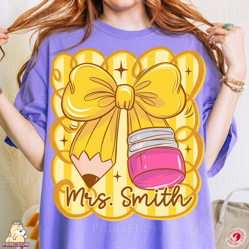 May include: A lilac-colored t-shirt featuring a large graphic of a yellow pencil with a bow, a pink jar, and the text "Mrs. Smith" in a playful font. The design is set against a yellow and white striped background.