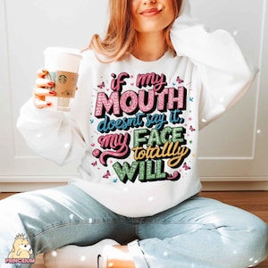 May include: White sweatshirt with a colorful graphic that says "If my mouth doesn't say it, my face totally will."