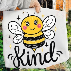 May include: White fabric with a cartoon bee illustration. The bee is yellow and black with white wings, pink cheeks, and a smiling face. The word "Kind" is written in black script below the bee, with star accents.