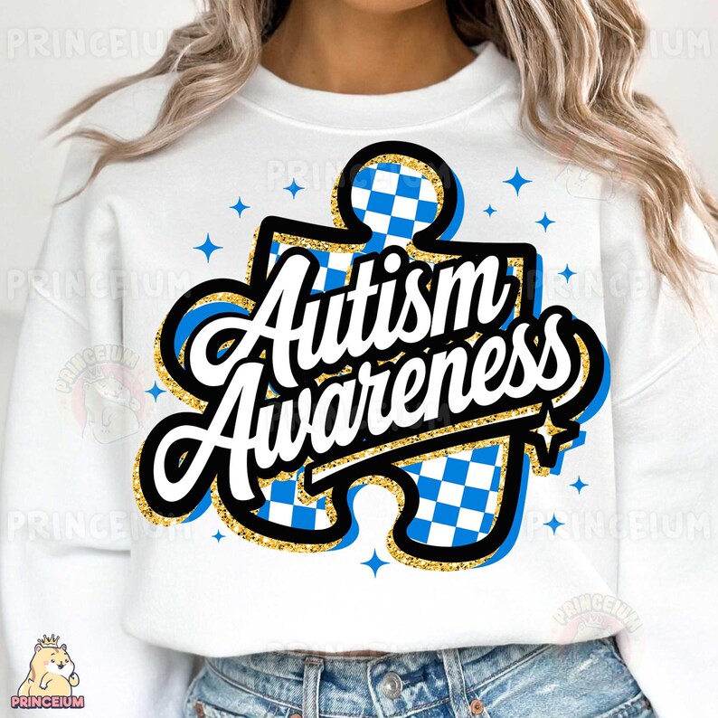 May include: White sweatshirt featuring a blue and white chequered jigsaw piece design. The words "Autism Awareness" are written in a gold glitter font on the jigsaw piece.