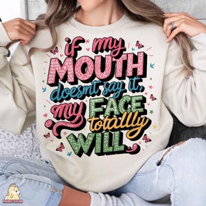 May include: A cream-colored sweatshirt with a colorful graphic print that reads "If my mouth doesn't say it, my face totally will."