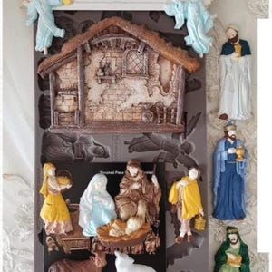 Puede incluir: Un juego de moldes decorativos para crear una escena de la Natividad. El juego incluye un establo detallado, ángeles y figuras de María, José y el niño Jesús, además de otros personajes. El molde mide 12.7cm x 25.4cm.