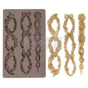 May include: A decorative mold and casted embellishments featuring floral and bow designs. The mold is a muted brown color, while the casted pieces are gold. The designs include flowers, leaves, and bows, suitable for crafting and decor projects.