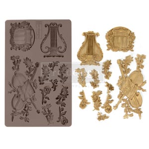 Könnte beinhalten: Eine Silikonform und gegossene Harzverzierungen zum Thema Musik. Die Form ist taupefarben und zeigt eine Leier, eine Geige und florale Designs. Die gegossenen Harzteile sind goldfarben und umfassen eine Leier, ein Schild, eine Geige und florale Akzente.