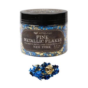 Könnte beinhalten: Ein durchsichtiger Kunststoffbehälter mit schwarzem Deckel, gefüllt mit feinen blauen und goldenen Metallic-Flocken. Das Etikett trägt die Aufschrift Art Ingredients Fine Metallic Flakes New York 150 ml. Vor dem Behälter liegt ein kleiner Haufen Flocken.