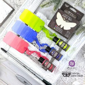 Può includere: Tre bottiglie di vernice acrilica liquida Prima Marketing nei colori lampone, pervinca e verde lime. Le bottiglie sono etichettate con il colore della vernice e il logo Prima Marketing. La vernice fa parte del Juicy Set, un set di vernici in edizione limitata.