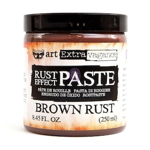 以下が含まれることがあります： Finnabair Art Extra Vaganceのラストエフェクトペースト（Brown Rust）が入った円筒形の瓶。ラベルにはRust Effect Paste、Brown Rust、250mlと記載されています。黒いスクリューキャップが付いており、中には濃い茶色のペーストが入っています。