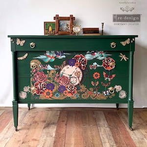 May include: A green dresser with two drawers features a whimsical design with a clock, flowers, butterflies, and dragonflies. The dresser has gold hardware and is decorated with a vintage aesthetic.