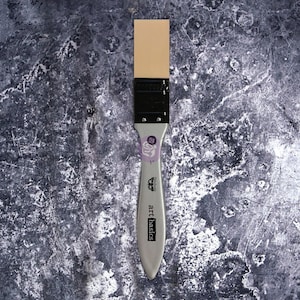 May include: A 1-inch wide art basics palette knife with a light tan blade and a silver handle. The handle has the text "art basics" printed on it. The brush is on a textured gray surface.