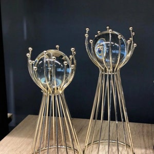 Può includere: Due supporti decorativi in metallo dorato con un globo di vetro rotondo in cima. I supporti hanno la forma di un cono con un design a rete metallica.