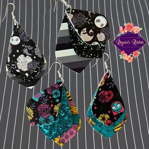 May include: Three pairs of dangle earrings featuring a layered design. The earrings are made of black faux leather with various patterns, including a black and white striped pattern, a floral pattern, and a pattern with a character from the movie 'The Nightmare Before Christmas'. The earrings are accented with turquoise glitter.