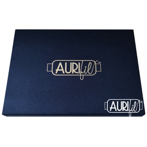 Op de afbeelding: Een marineblauwe rechthoekige doos met de gouden tekst "AURIfil" op de bovenkant. De doos heeft een getextureerd oppervlak en een kleinere versie van het logo in de rechter benedenhoek.