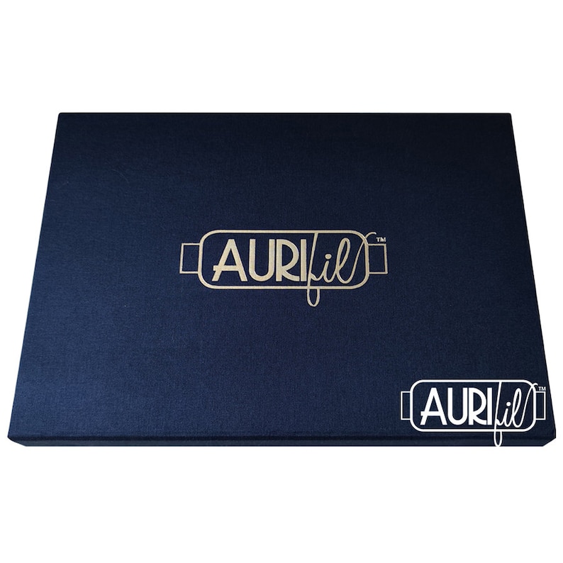 Op de afbeelding: Een marineblauwe rechthoekige doos met de gouden tekst "AURIfil" op de bovenkant. De doos heeft een getextureerd oppervlak en een kleinere versie van het logo in de rechter benedenhoek.