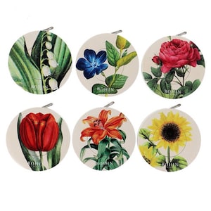 Könnte beinhalten: Sechs runde, weiße Maßbänder mit Blumenmuster. Jedes Band zeigt eine andere Blume: Maiglöckchen, blaue Blume, Rose, Lilie, Sonnenblume und Tulpe. Die Bänder sind alle mit "BOHIN PARIS" beschriftet.