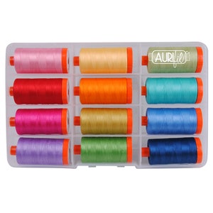 Puede incluir: Una caja de almacenamiento de plástico transparente con 12 carretes de hilo Aurifil. Los carretes están dispuestos en tres filas de cuatro. Los colores del hilo son rosa, naranja, rojo, fucsia, morado, amarillo, verde, azul, turquesa, azul claro, azul oscuro y beige.