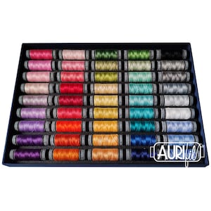 Könnte beinhalten: Eine Schachtel mit 36 Spulen Aurifil-Garn in verschiedenen Farben. Die Spulen sind in Reihen und Spalten angeordnet, wobei jede Reihe eine andere Farbe enthält. Die Schachtel ist aus blauem Karton und trägt das Aurifil-Logo auf der Vorderseite.
