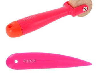 May include: A pink and orange sewing tool with a wooden roller and a pink plastic tool with a pointed end. Both tools have the Bohin Paris logo.