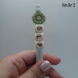 May include: A silver pen with a green flower charm and white letter beads spelling "SLIP".